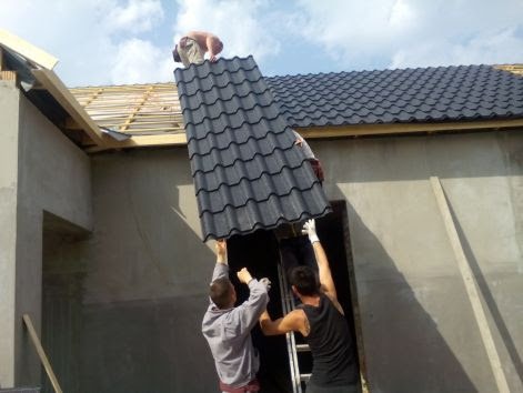 Trzech dekarzy montuje metalową blachodachówkę na dachu nowego budynku, widoczny ruszt drewniany i częściowo pokryty dach.