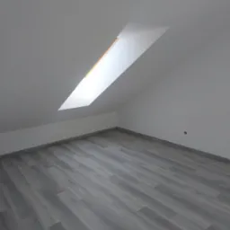 Poddasze z nową, szarą podłogą imitującą drewno. W dachu okno połaciowe wpuszczające jasne światło. Ściany pomalowane na biało, widoczny fragment gniazdka.