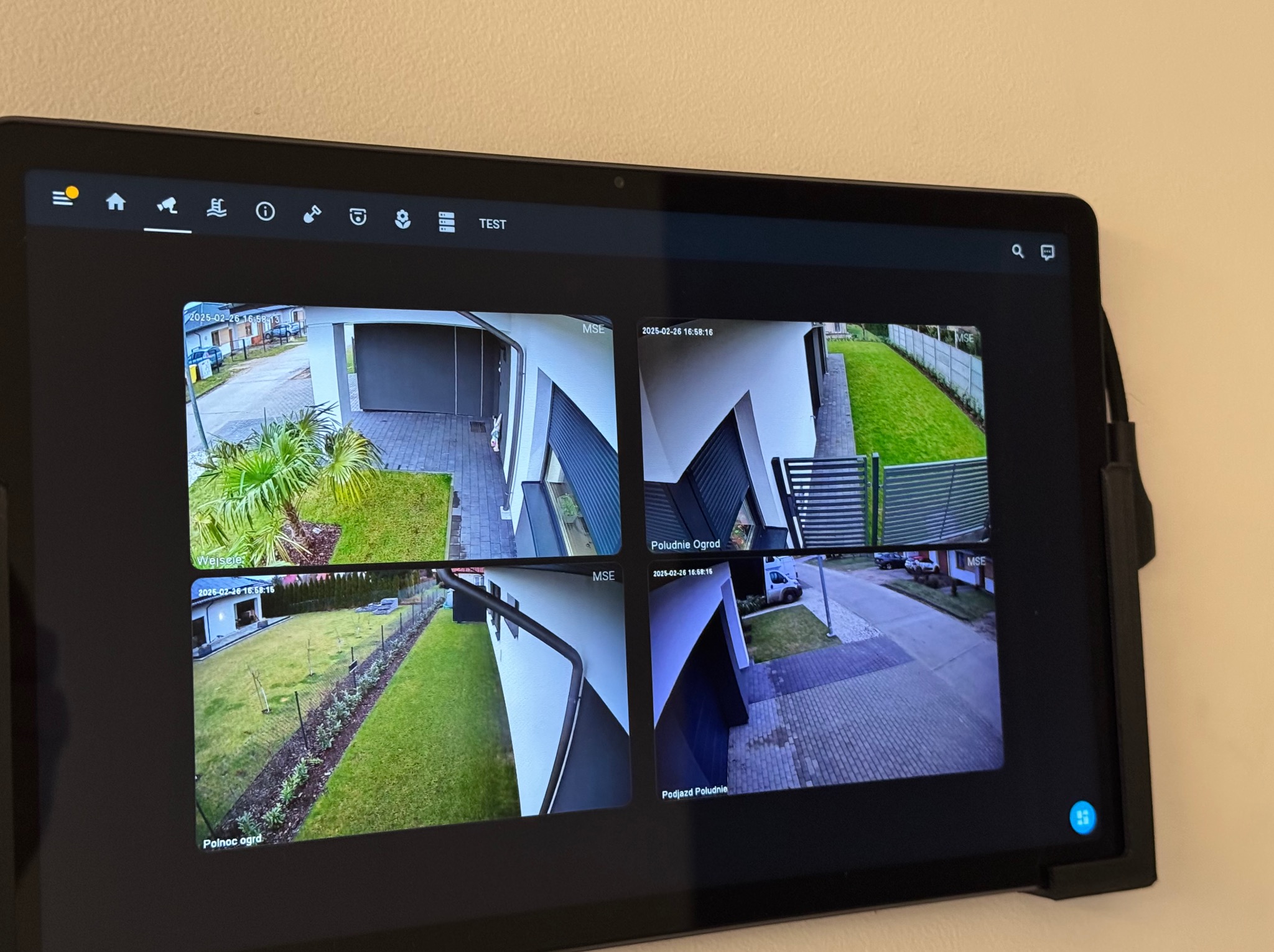 Ekran tabletu prezentujący podgląd z czterech kamer monitoringu wizyjnego, ukazujących wejście do domu, południową część ogrodu, północną część ogrodu oraz podjazd.