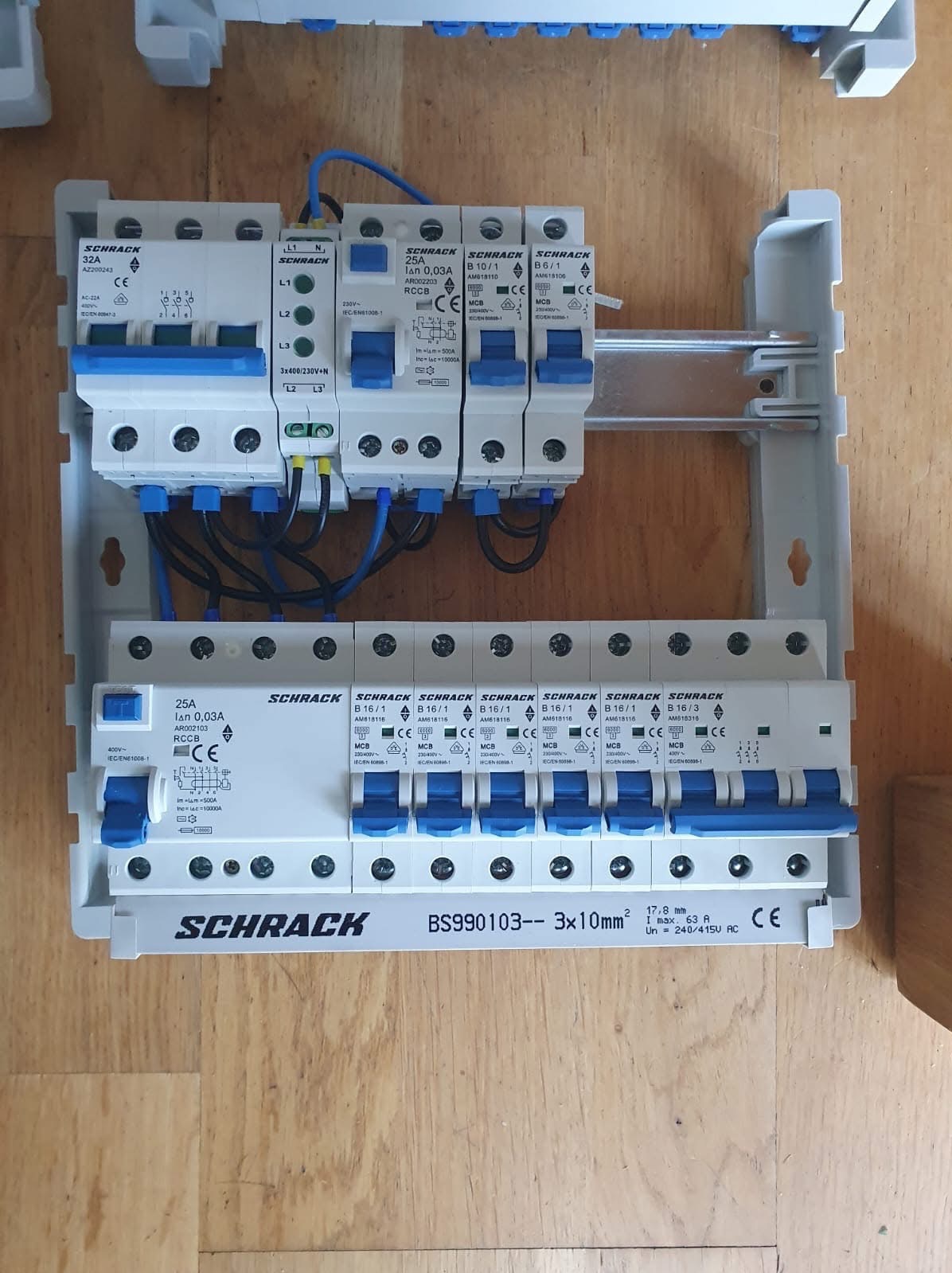 Rozdzielnica elektryczna marki Schrack z zainstalowanymi bezpiecznikami i wyłącznikami różnicowoprądowymi, widoczne okablowanie i oznaczenia na urządzeniach, zamontowana w obudowie z tworzywa...