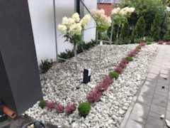 Ogród z białymi kamieniami, ozdobnymi krzewami i ścieżką z kostki brukowej, widok z góry.