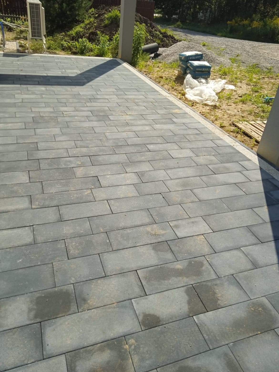 Ułożona szara nawierzchnia z prostokątnych elementów, widoczne worki z cementem i paleta w tle, jasna obwódka nawierzchni.