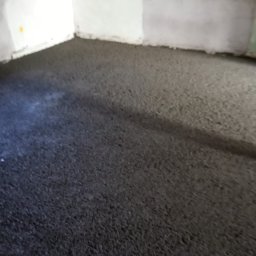 Grzegorz Zieliński Em-Bud Cieszyn - Wylana, szara posadzka w surowym wnętrzu z białymi ścianami z betonu komórkowego. Widoczne ślady po pracach budowlanych, surowy stan wykończenia.