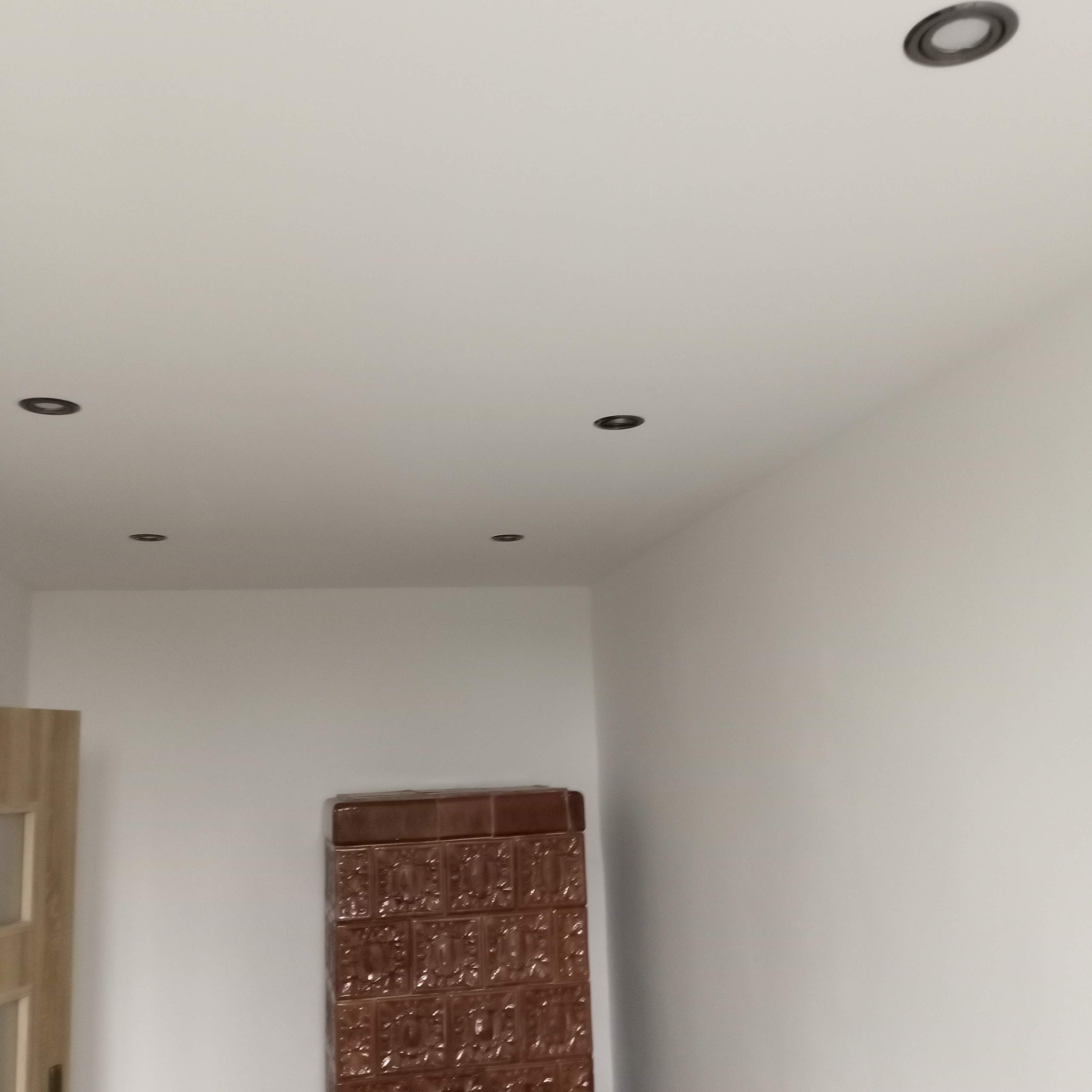 Świeżo pomalowane wnętrze z brązowym piecem kaflowym i zamontowanymi punktowymi lampami sufitowymi.