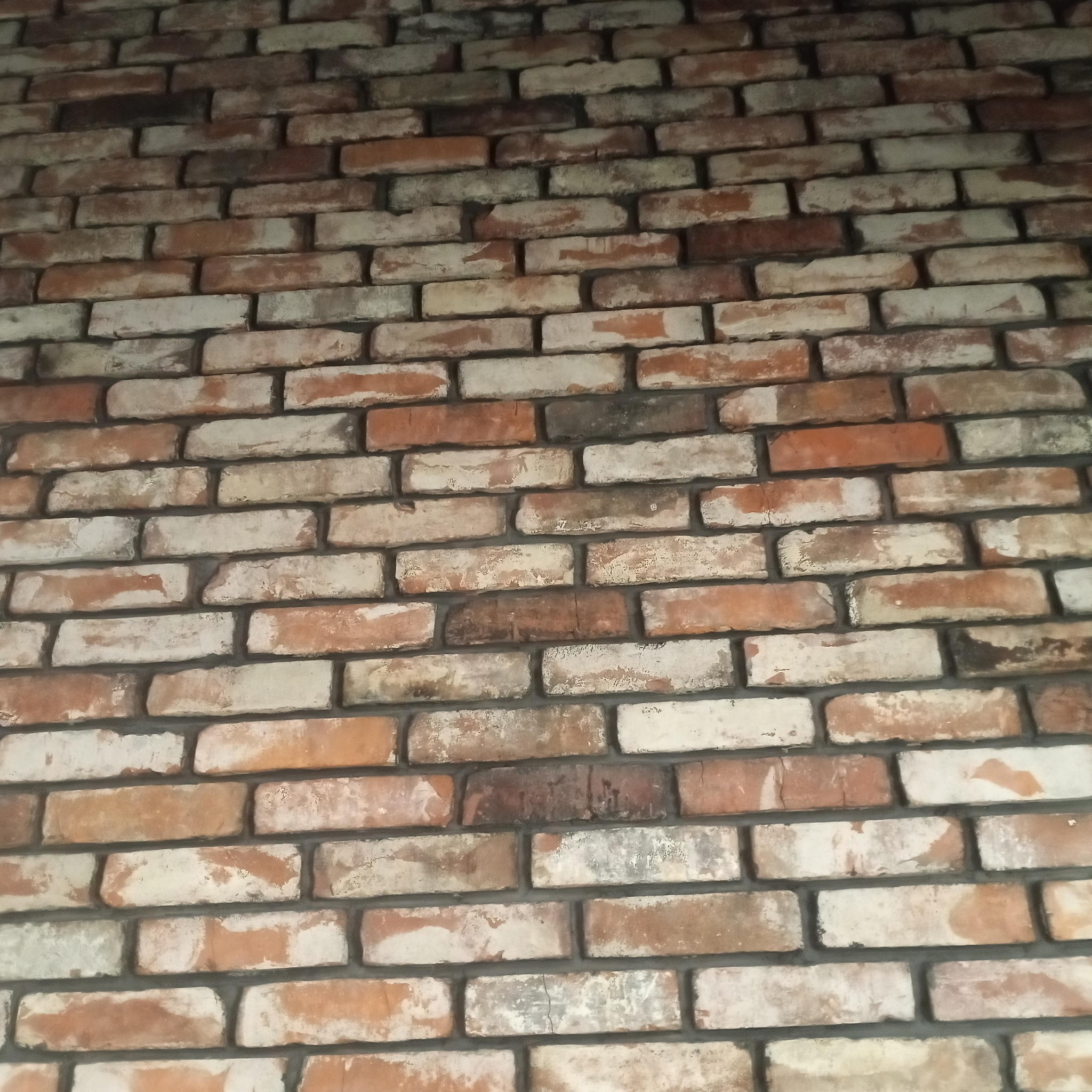 Tekstura ściany z cegły klinkierowej w odcieniach bieli, pomarańczy i brązu, z widocznymi fugami, imitująca starą cegłę.
