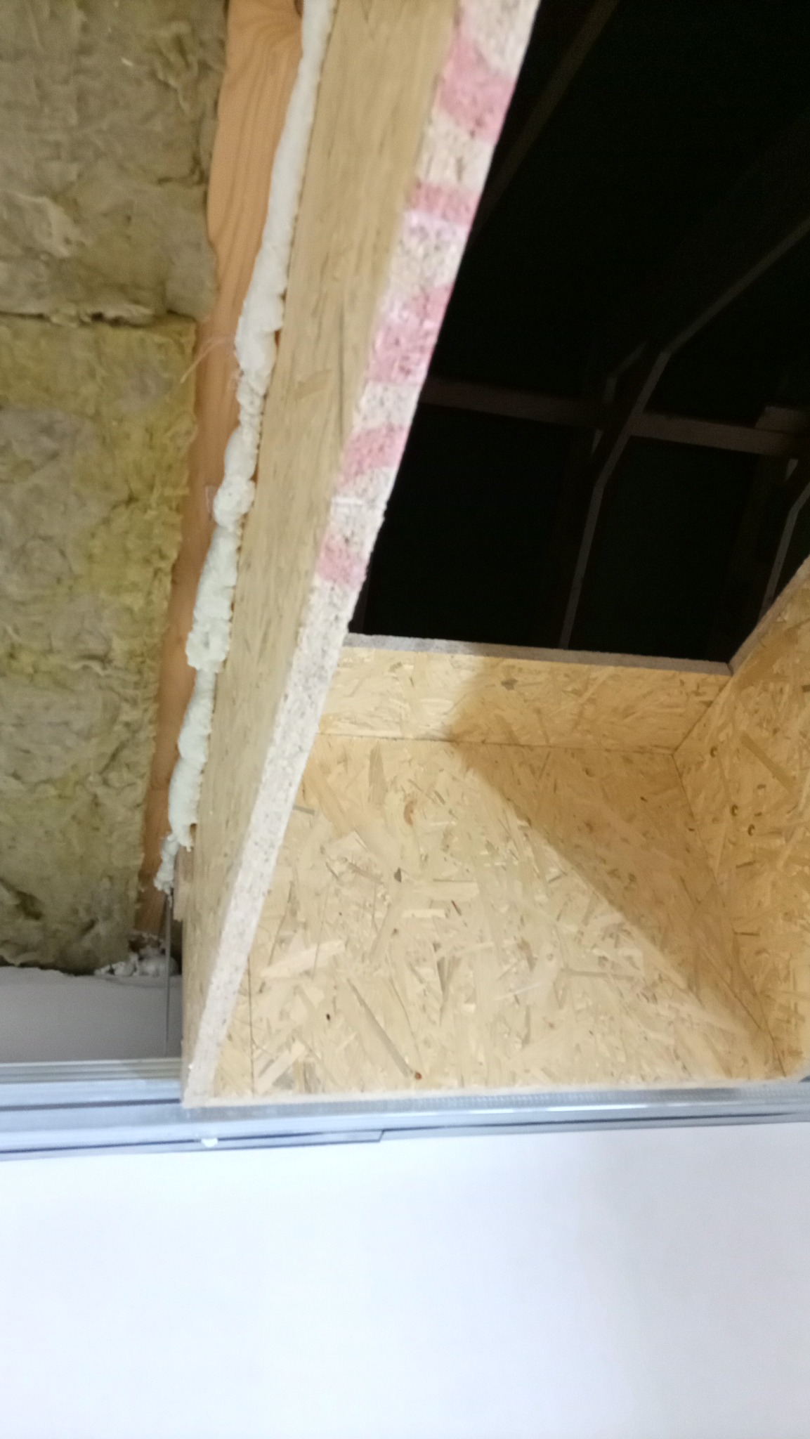 Ocieplenie poddasza wełną mineralną i obudowa z płyty OSB, widoczne pianowanie szczelin. Prace wykończeniowe w trakcie realizacji, surowy stan.