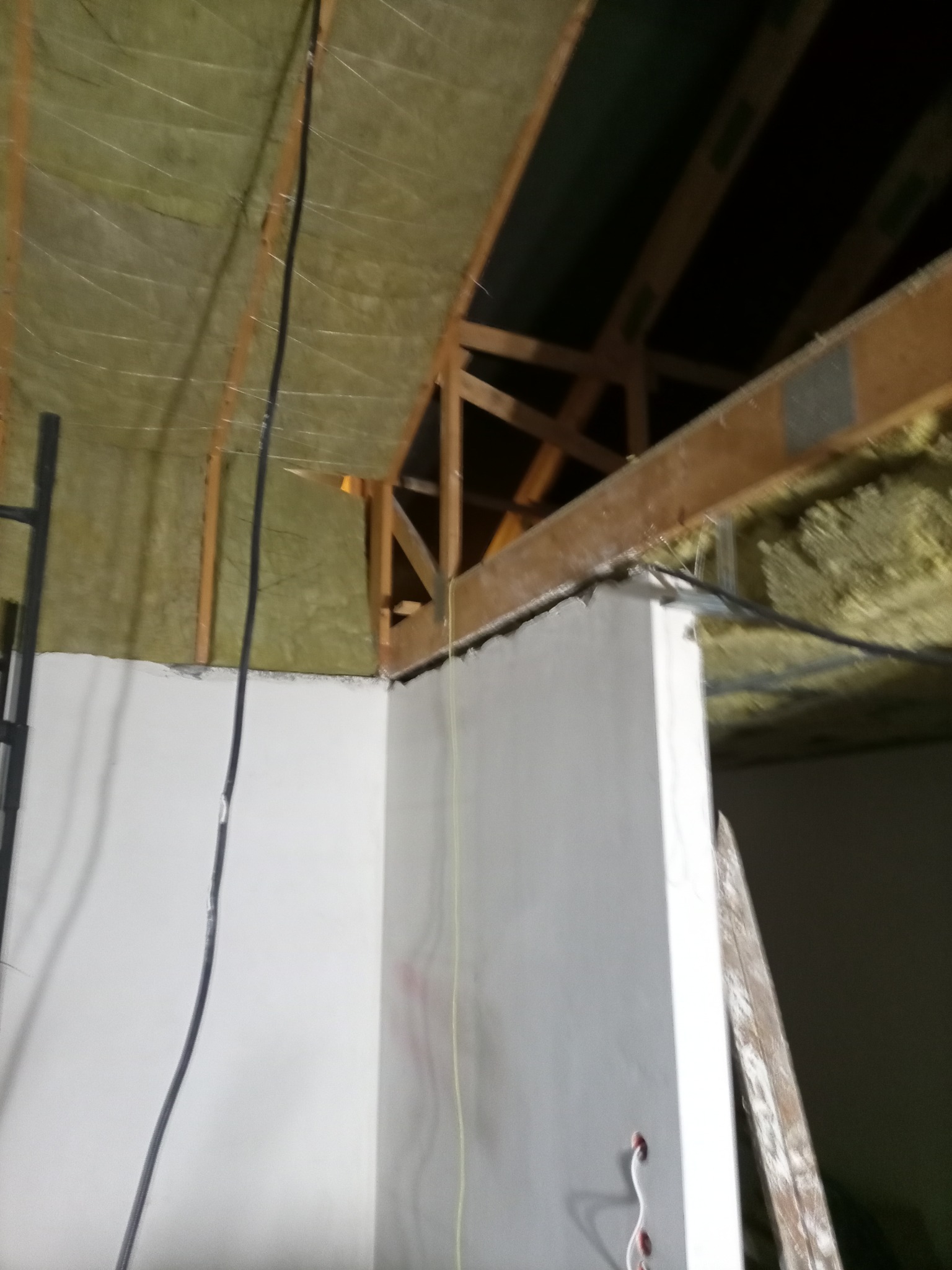 Ściana po gładziowaniu, widoczne kable i fragment izolacji poddasza. Prace wykończeniowe w surowym wnętrzu, drabina oparta o ścianę.