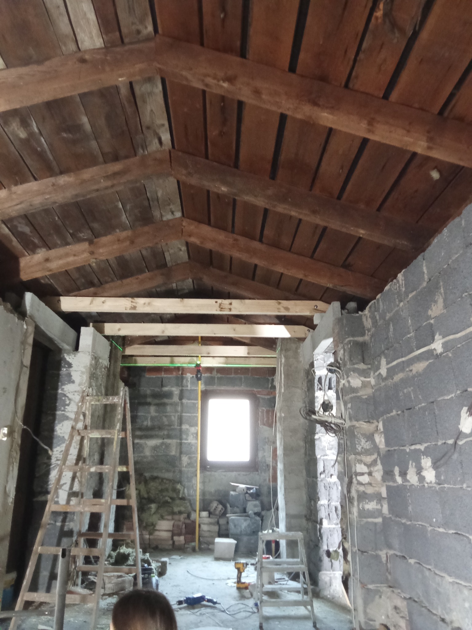Surowe wnętrze w Cieszynie z drewnianym stropem i surowymi ścianami z betonu komórkowego. Widoczne rusztowania i okno w tle. Wnętrze w trakcie prac remontowych.