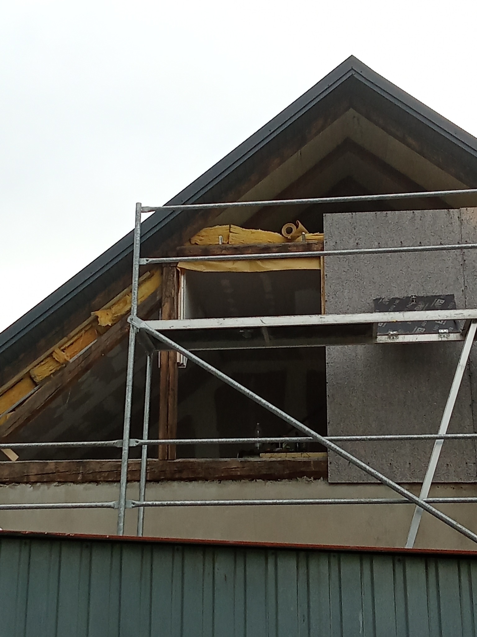 Ocieplanie poddasza wełną mineralną, widoczne rusztowanie i płyta OSB. Prace wykończeniowe na etapie izolacji termicznej dachu. Detal z budowy.