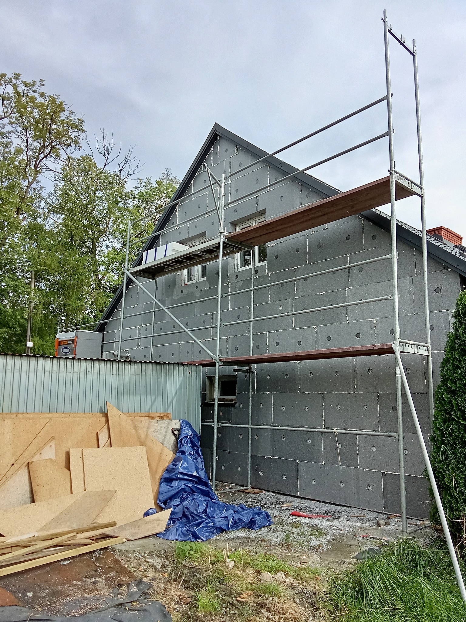 Dom w trakcie ocieplania styropianem, widoczne rusztowanie i materiały budowlane. Etap prac przed nałożeniem tynku.