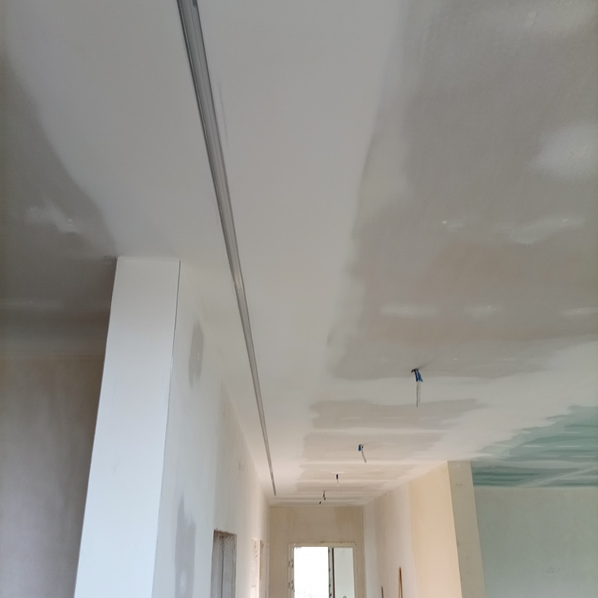 Sufit po montażu profili i częściowym położeniu gładzi, widoczne łączenia płyt. Prace wykończeniowe w jasnym wnętrzu z oknem w tle.