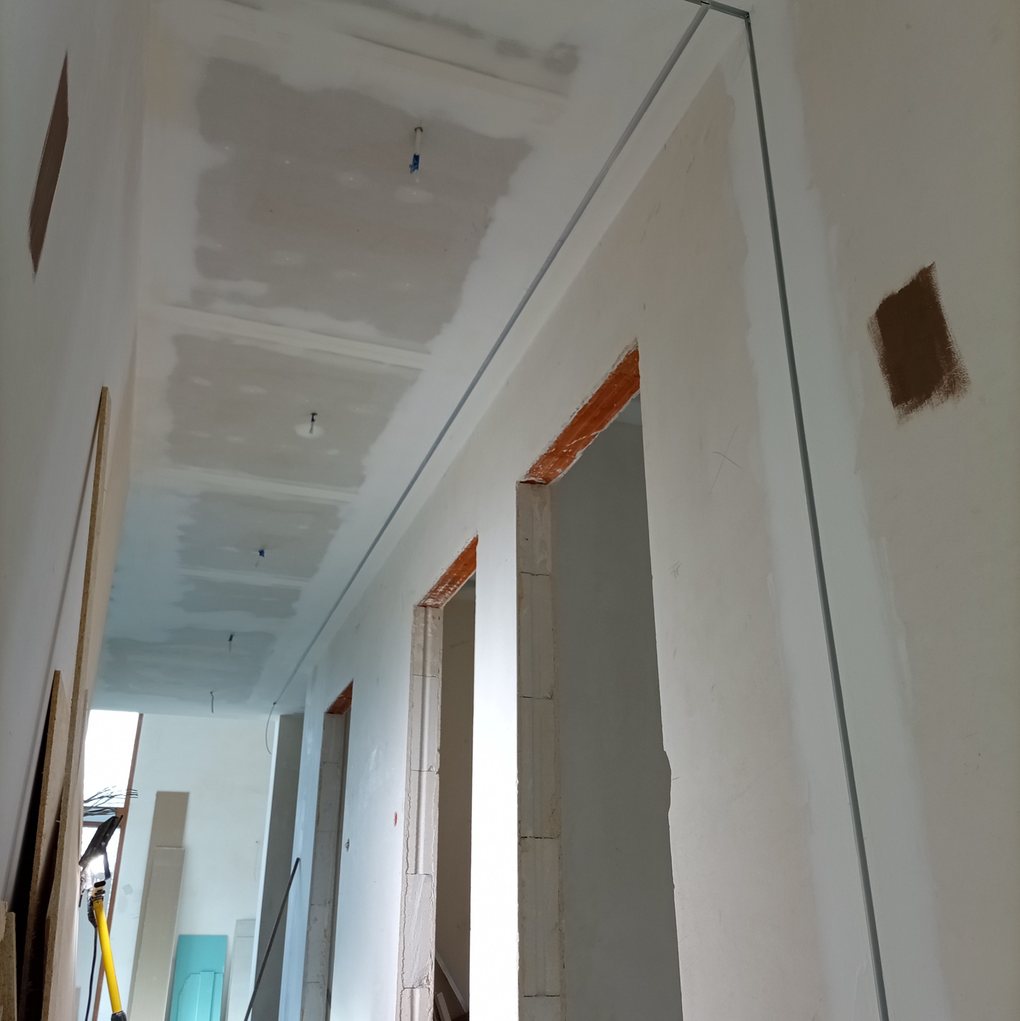 Korytarz w trakcie prac wykończeniowych: ściany z fragmentami gładzi, widoczne profile, sufit z płyt kartonowo-gipsowych, przygotowane do dalszych prac.