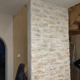 LUX - REM ŁUKASZ NIEDBALSKI - Ściana wykończona dekoracyjnym kamieniem w odcieniach beżu i bieli, widoczna część klatki schodowej i fragment wieszaka z ubraniem.