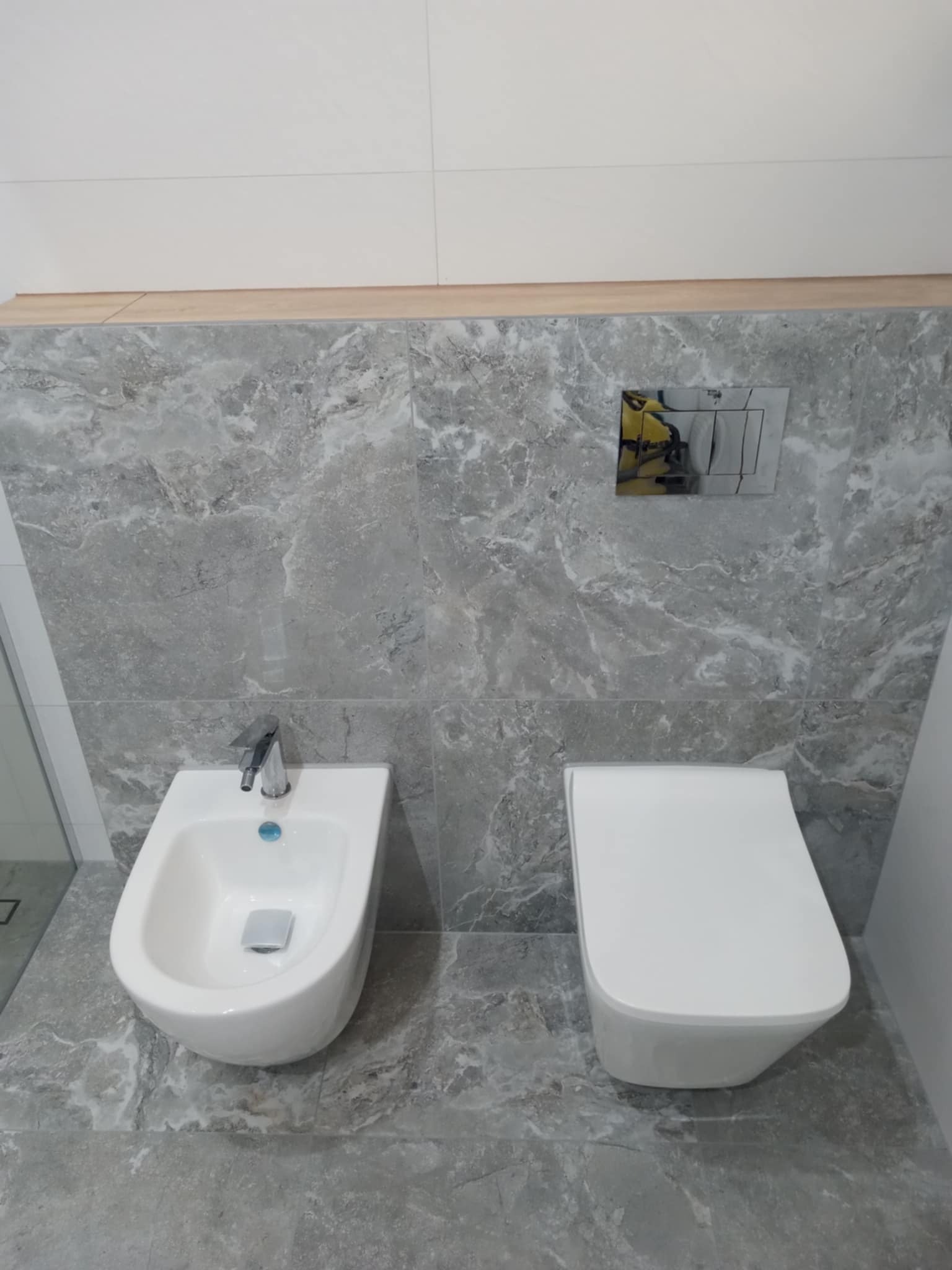Nowoczesna łazienka: biała toaleta i bidet na tle marmurowych płytek ściennych i podłogowych. Minimalistyczny design, chromowana armatura, subtelne oświetlenie.