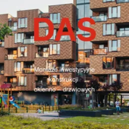 Nowoczesny budynek mieszkalny z licznymi oknami i balkonami, z dużym czerwonym napisem 'DAS' nałożonym na fasadę, widok z poziomu trawnika z placem zabaw w tle.