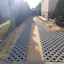 MARIO-BRUK MARIUSZ ZBORALSKI - Układanie ażurowych płyt betonowych na podjeździe, widoczny piasek pomiędzy płytami, dom w tle, mężczyzna oparty o murek.