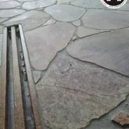 Kamienna posadzka z odpływem liniowym, widoczny logotyp firmy w prawym górnym rogu.