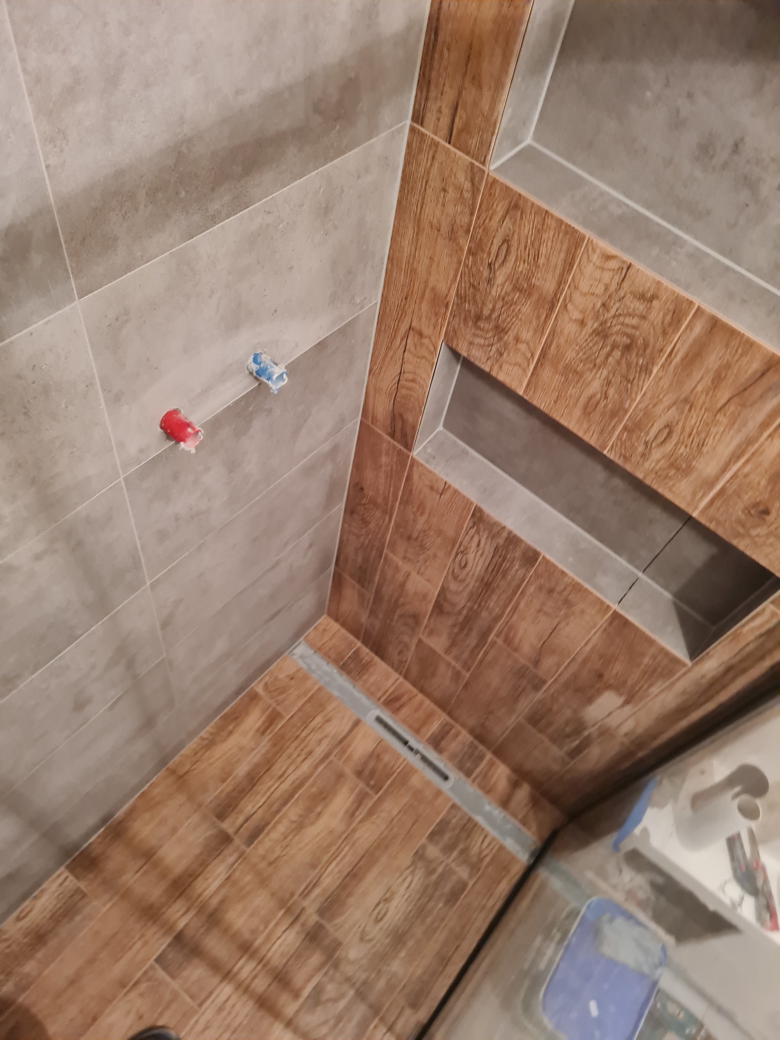 Wykończona kabina prysznicowa w Zielonej Górze z odpływem liniowym i wnęką w ścianie, wyłożona płytkami imitującymi drewno oraz szarymi płytkami na ścianach.