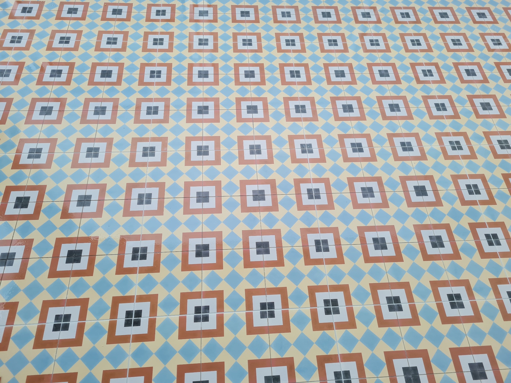 Wzorzysta podłoga z płytek w odcieniach błękitu, beżu, brązu i bieli, ułożona w powtarzalny geometryczny deseń kwadratów i rombów.