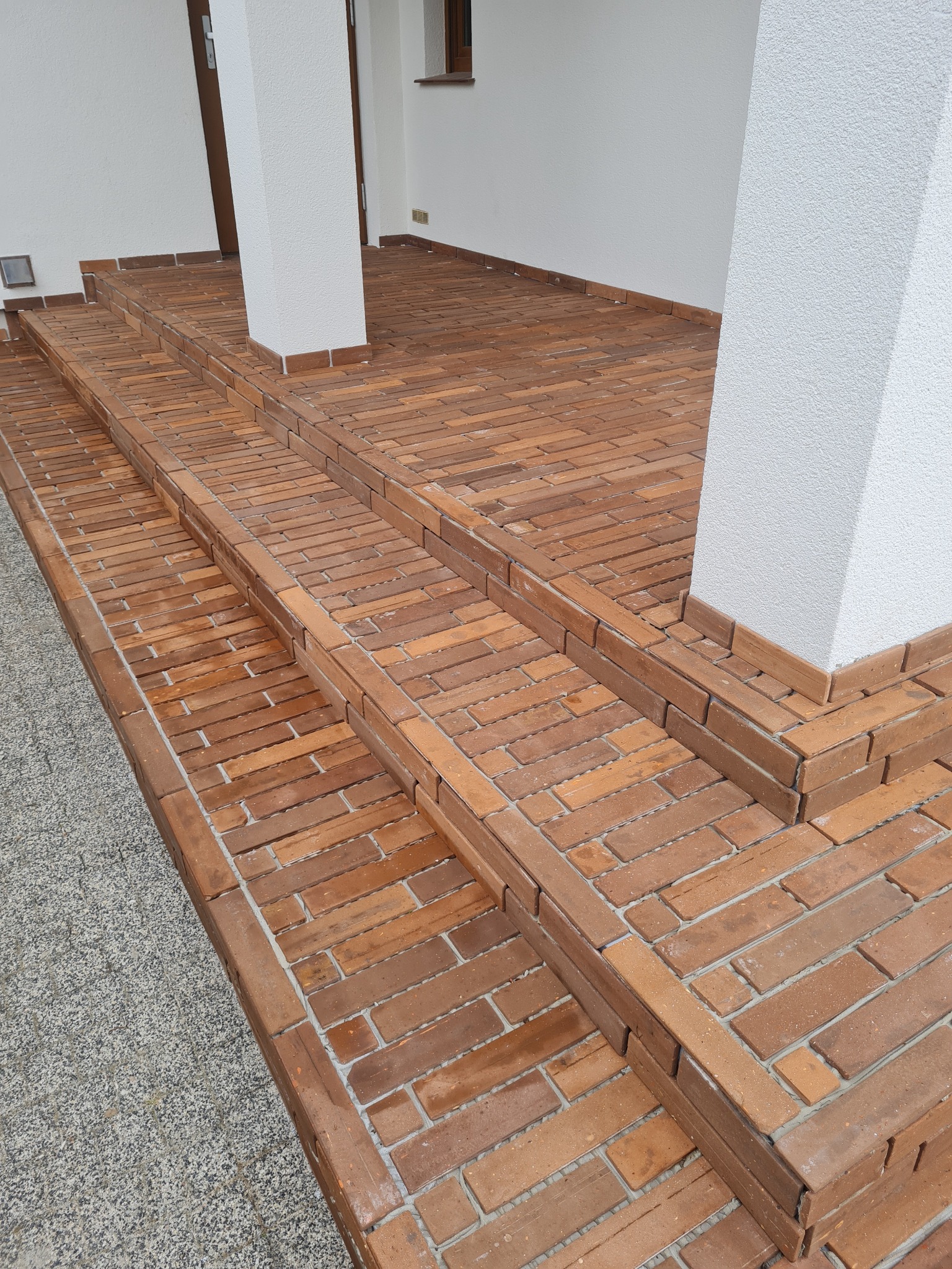 Wykończone schody wejściowe z cegły klinkierowej, prowadzące do budynku z białymi kolumnami i szarym chodnikiem.