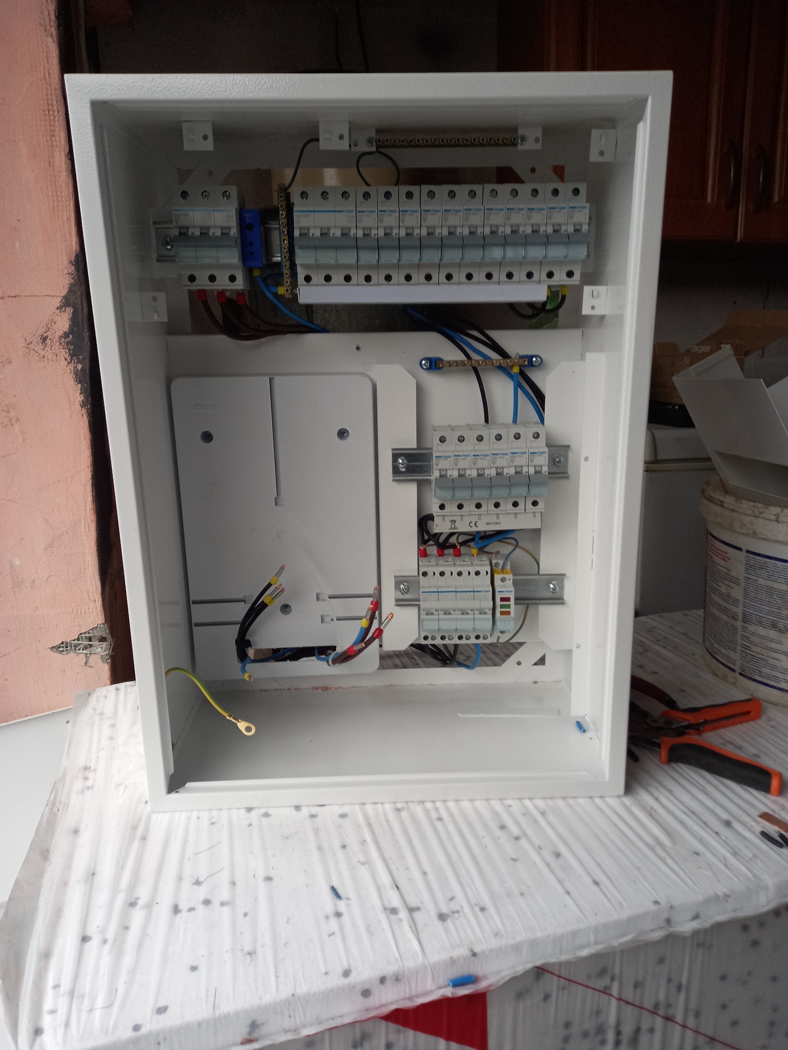 Otwarta, biała skrzynka rozdzielcza z zamontowanymi bezpiecznikami i przewodami, widoczne narzędzia obok.