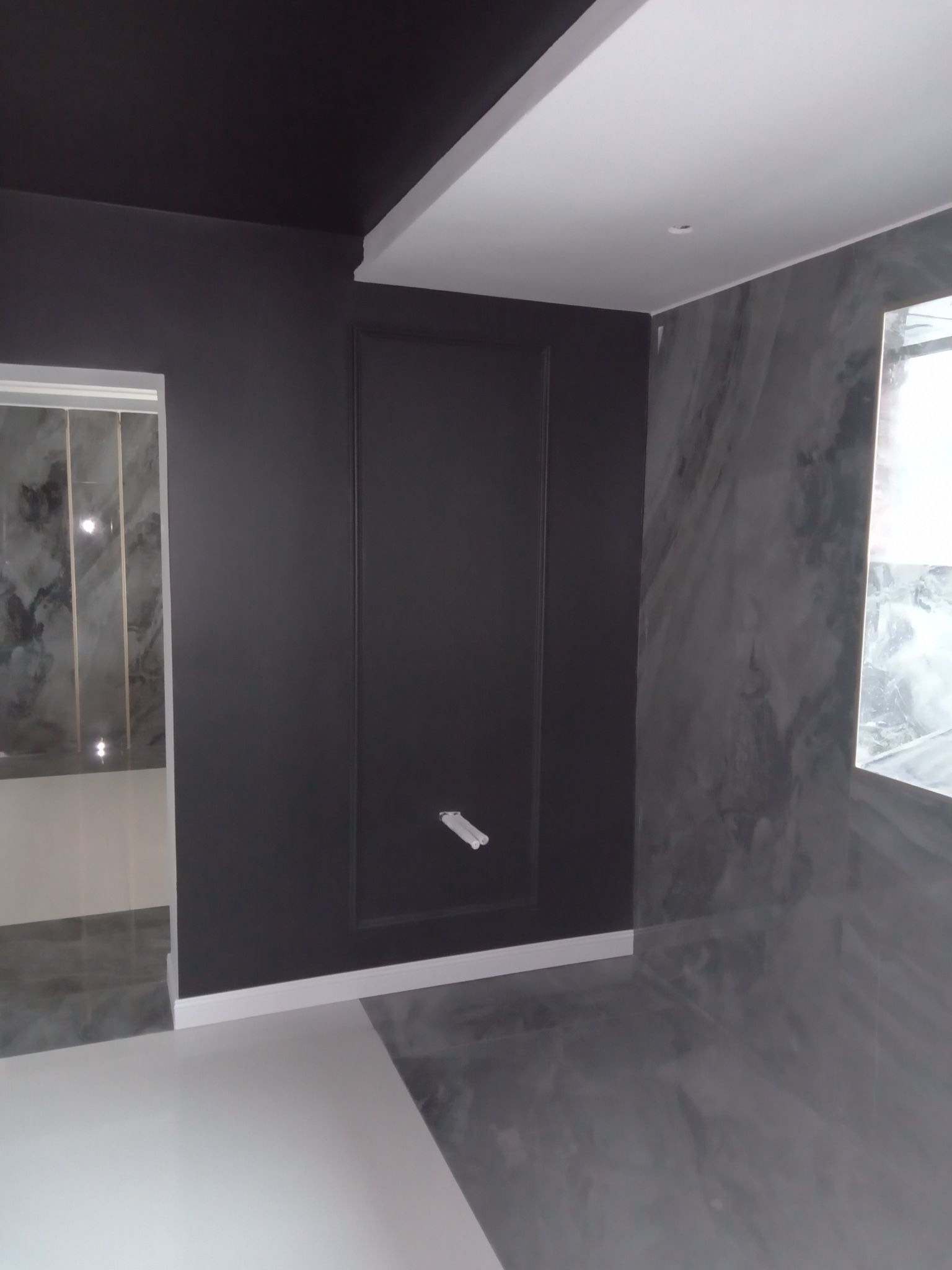 Wnętrze po remoncie: Czarna ściana z dekoracyjną ramą, marmurowe płytki i biała podłoga w nowoczesnym stylu.