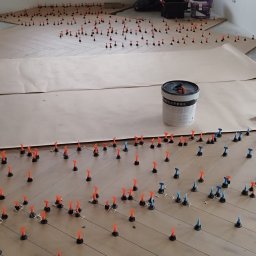 Paweł Gawron - Układanie parkietu w jodełkę z użyciem systemu poziomowania płytek. Widoczny glazurnik i wiadro z klejem. Podłoga zabezpieczona papierem. Jasne wnętrze z oknem.