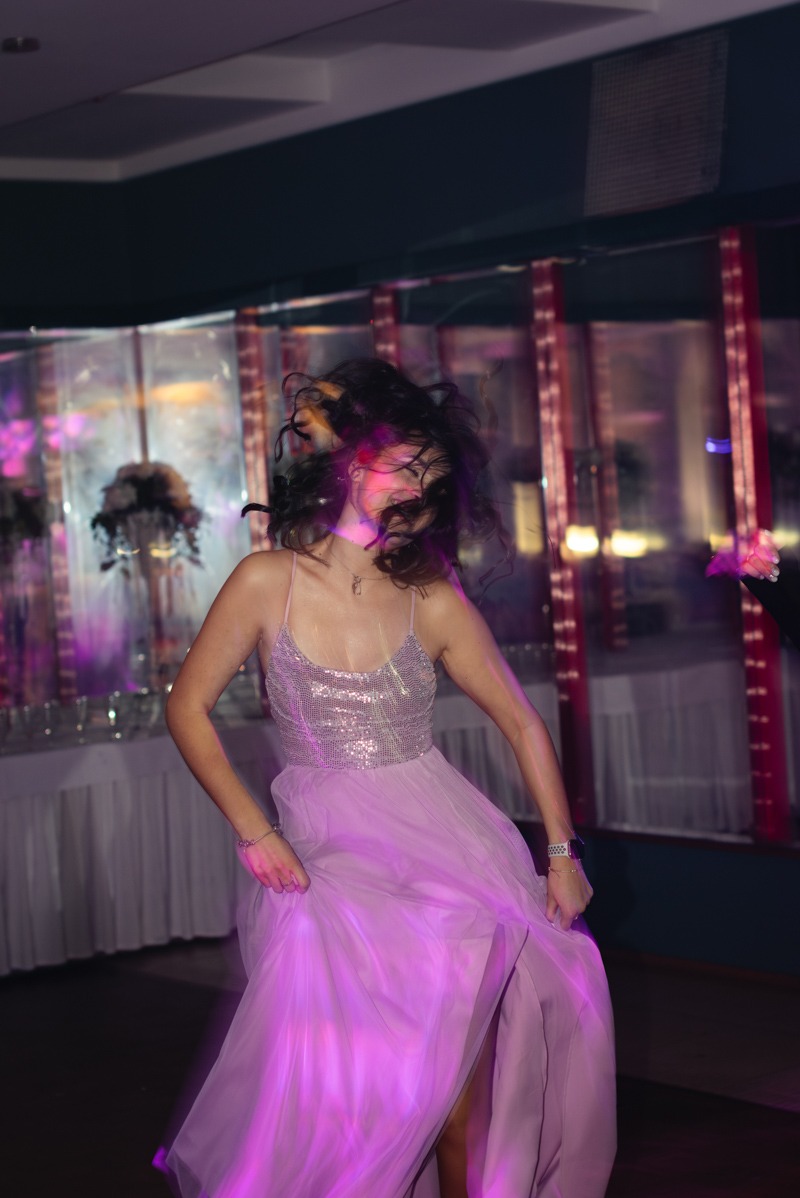 Młoda kobieta w brokatowej sukience tańczy na imprezie, rozmycie ruchu, fioletowe oświetlenie.