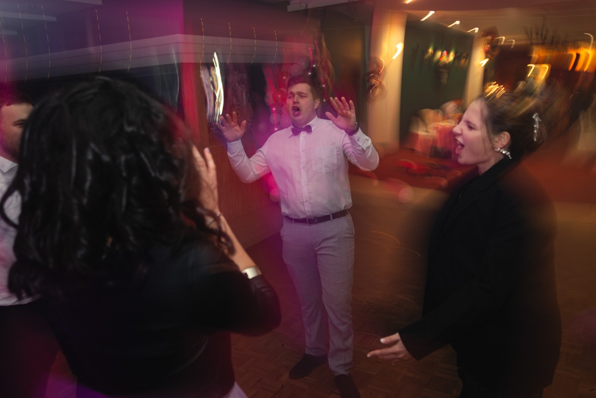 Rozmazane ujęcie trzech osób śpiewających lub krzyczących na parkiecie podczas imprezy z efektami świetlnymi.