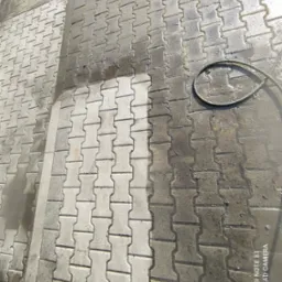 Częściowo wyczyszczona kostka brukowa z widoczną różnicą w kolorze między umytą a brudną powierzchnią, obok leży zwinięty wąż.