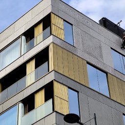 Grupa Doczyszczacze Monika Sosińska - Pracownik na linach zabezpieczających wykonuje prace na elewacji nowoczesnego budynku z elementami w kolorze złota i dużymi oknami, widoczny napis 'MARVIPOL' na elewacji.