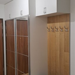 Lubomir Lubomir - Wnękowa szafa z przesuwnymi lustrzanymi drzwiami, połączona z panelem w kolorze drewna z wieszakami i szafką z siedziskiem w przedpokoju.