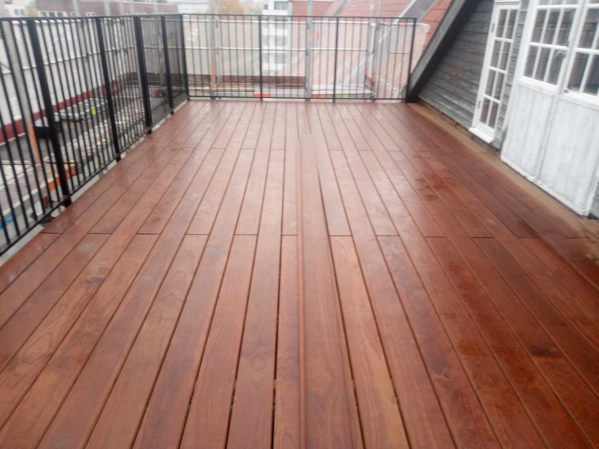 Nowy taras drewniany na dachu z czarną balustradą, widok na okoliczne budynki i białe drzwi balkonowe.