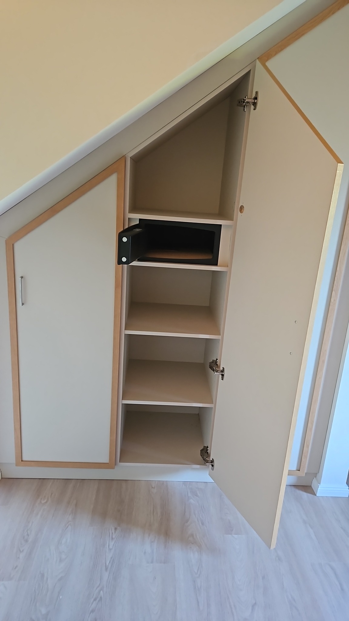 Wnękowa szafa z otwartymi drzwiami, z drewnianą ramą i sejfem w środku, na jasnej podłodze.