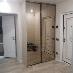 Dzmitry Sharakhouski - Jasne wnętrze przedpokoju z lustrzaną szafą przesuwną, widoczne drzwi wejściowe i wejście do łazienki z beżowymi płytkami.