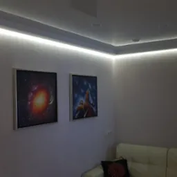 Pokój z podwieszanym sufitem z oświetleniem LED, na ścianie dwa obrazy przedstawiające motywy kosmiczne, narożnik sofy w rogu.