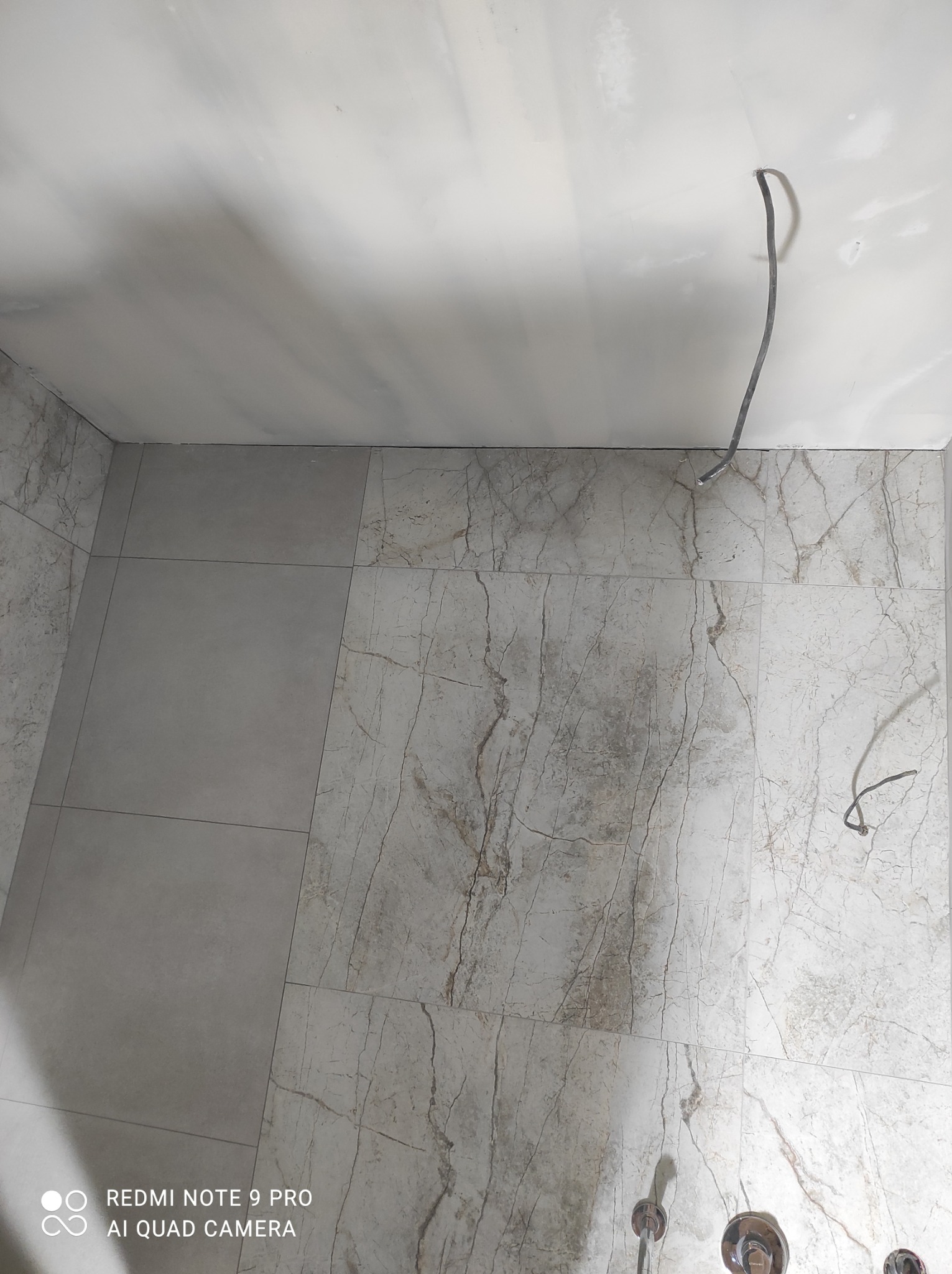 Świeżo położone płytki imitujące marmur na ścianach i podłodze łazienki, widoczne wystające kable ze ściany, przygotowanie do montażu armatury.