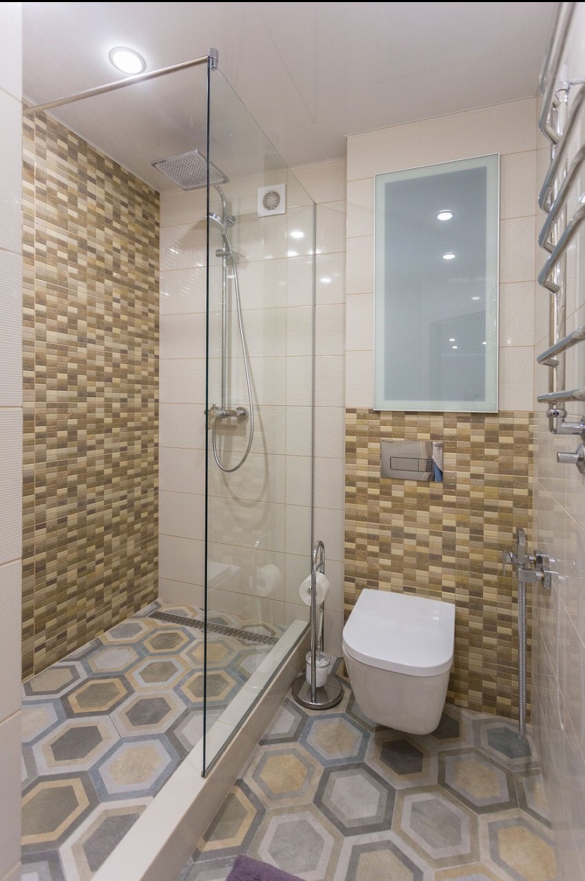 Nowoczesna łazienka z kabiną prysznicową typu walk-in, heksagonalną mozaiką podłogową w odcieniach szarości i beżu oraz toaletą wiszącą.