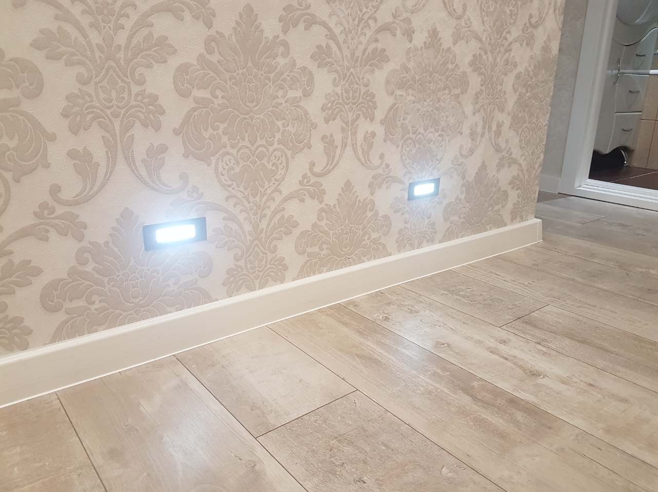 Wnętrze z podświetlanymi listwami przypodłogowymi i tapetą w ornamenty, podłoga imitująca drewno.