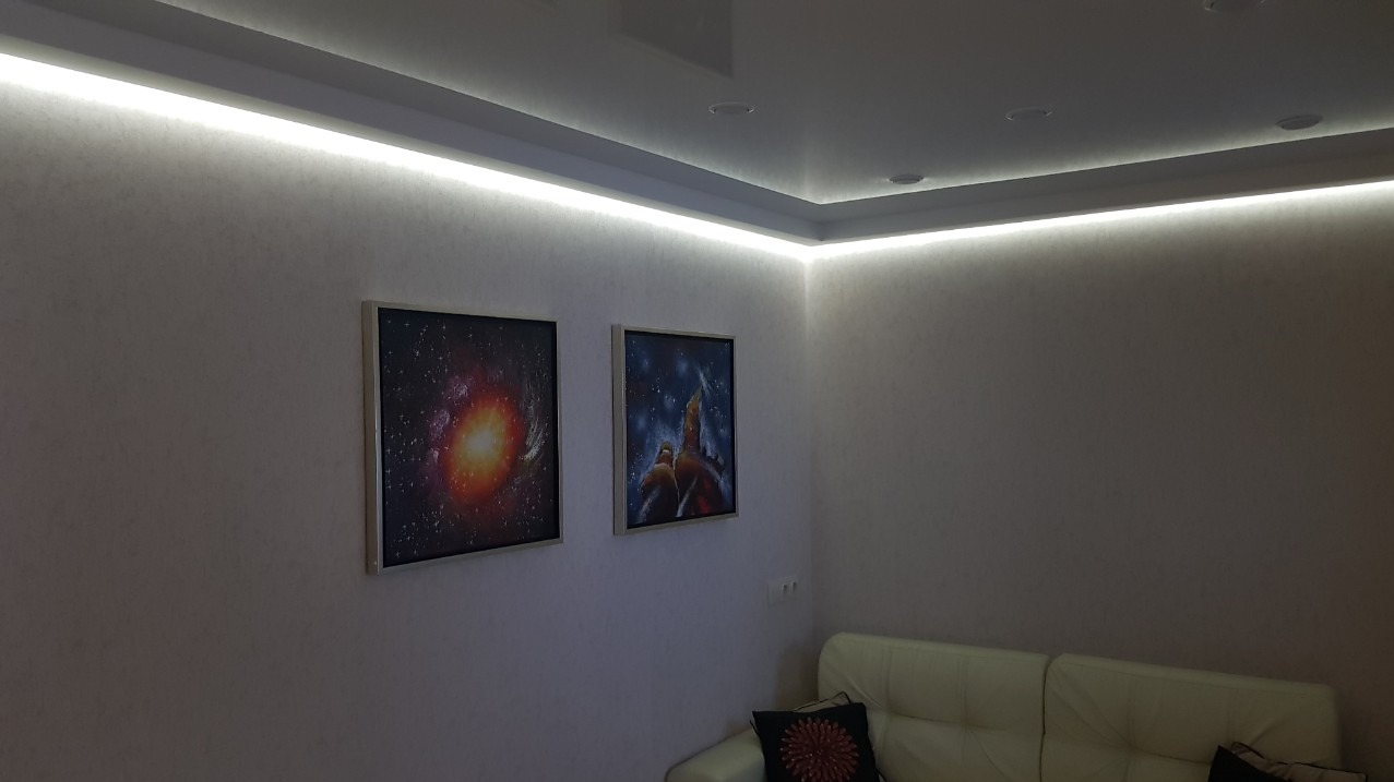 Pokój z podwieszanym sufitem z oświetleniem LED, na ścianie dwa obrazy przedstawiające motywy kosmiczne, narożnik sofy w rogu.