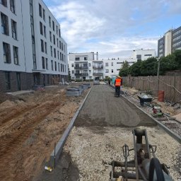 OL-BRUK OLEH TVERDOKHLIB - Prace ziemne w Warszawie: utwardzanie drogi dojazdowej na terenie budowy osiedla mieszkaniowego, widoczny ubijak wibracyjny i miniładowarka.