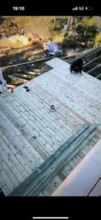 Wysoki kąt widzenia na drewniany szkielet dachu w trakcie budowy, z widocznym pracownikiem w ciemnej odzieży i elementami izolacji w tle.