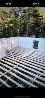 Wnętrze domu w trakcie budowy, widoczne ściany z płyt oraz drewniana konstrukcja podłogi, z zewnątrz widok na las.