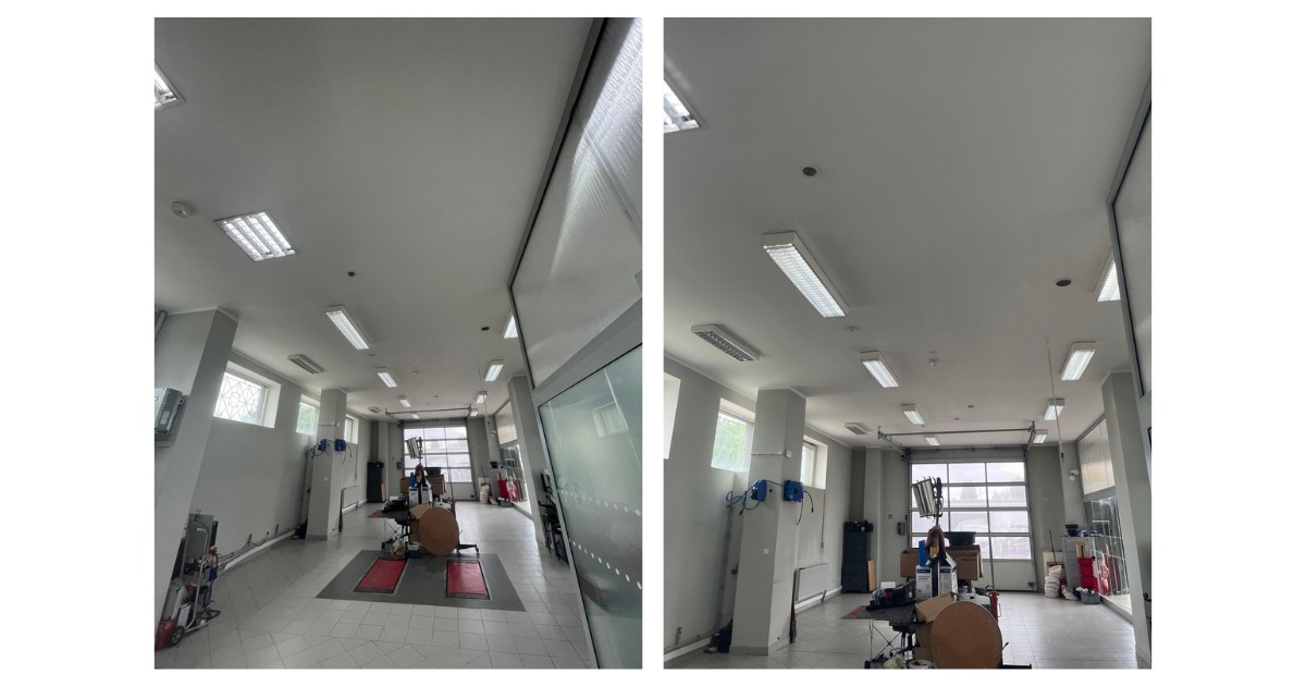 Wnętrze warsztatu samochodowego przed remontem, widok na sufit z oświetleniem, kolumny i bramę garażową. Widoczne narzędzia i wyposażenie warsztatowe.