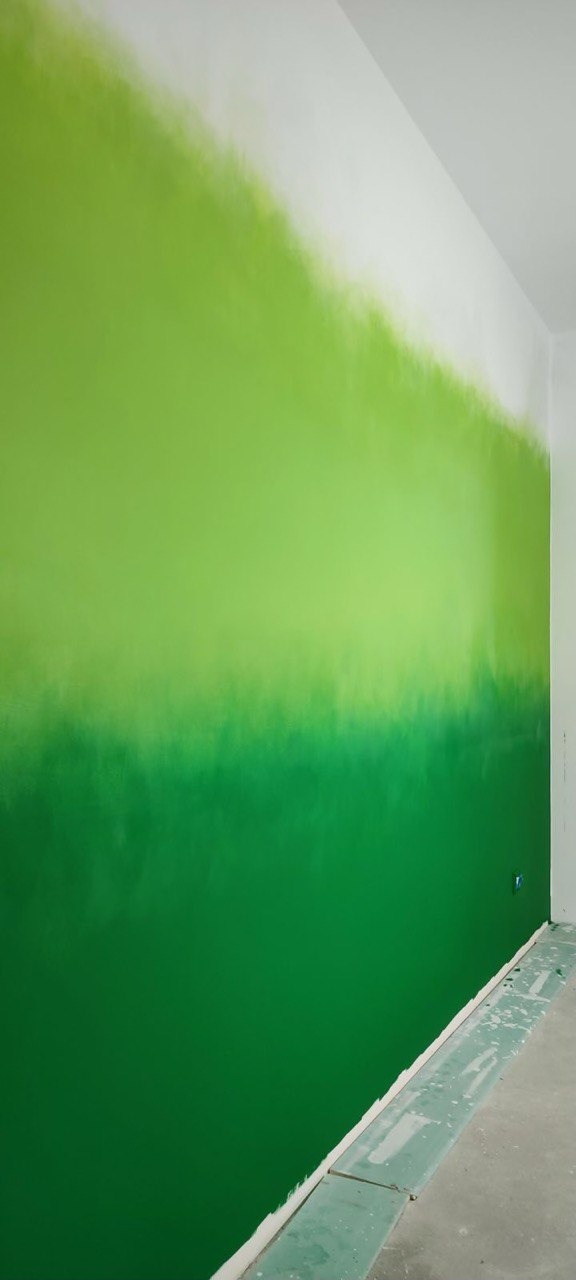 Ściana pomalowana farbą w odcieniach zieleni, przechodząca od ciemnego do jasnego, aż do bieli u góry. Widoczny fragment podłogi z zabezpieczeniem.