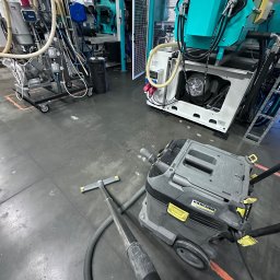 MuchiClean - Przemysłowy odkurzacz Karcher Professional na szarej betonowej posadzce hali produkcyjnej, w tle maszyny i instalacje.