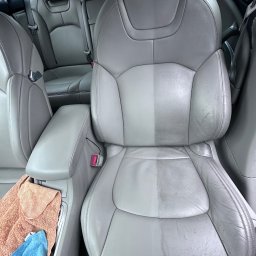 MuchiClean - Szare skórzane siedzenie samochodowe w trakcie czyszczenia, widoczna wyraźna różnica między wyczyszczoną a brudną częścią, obok leżą złożone ręczniki z mikrofibry.