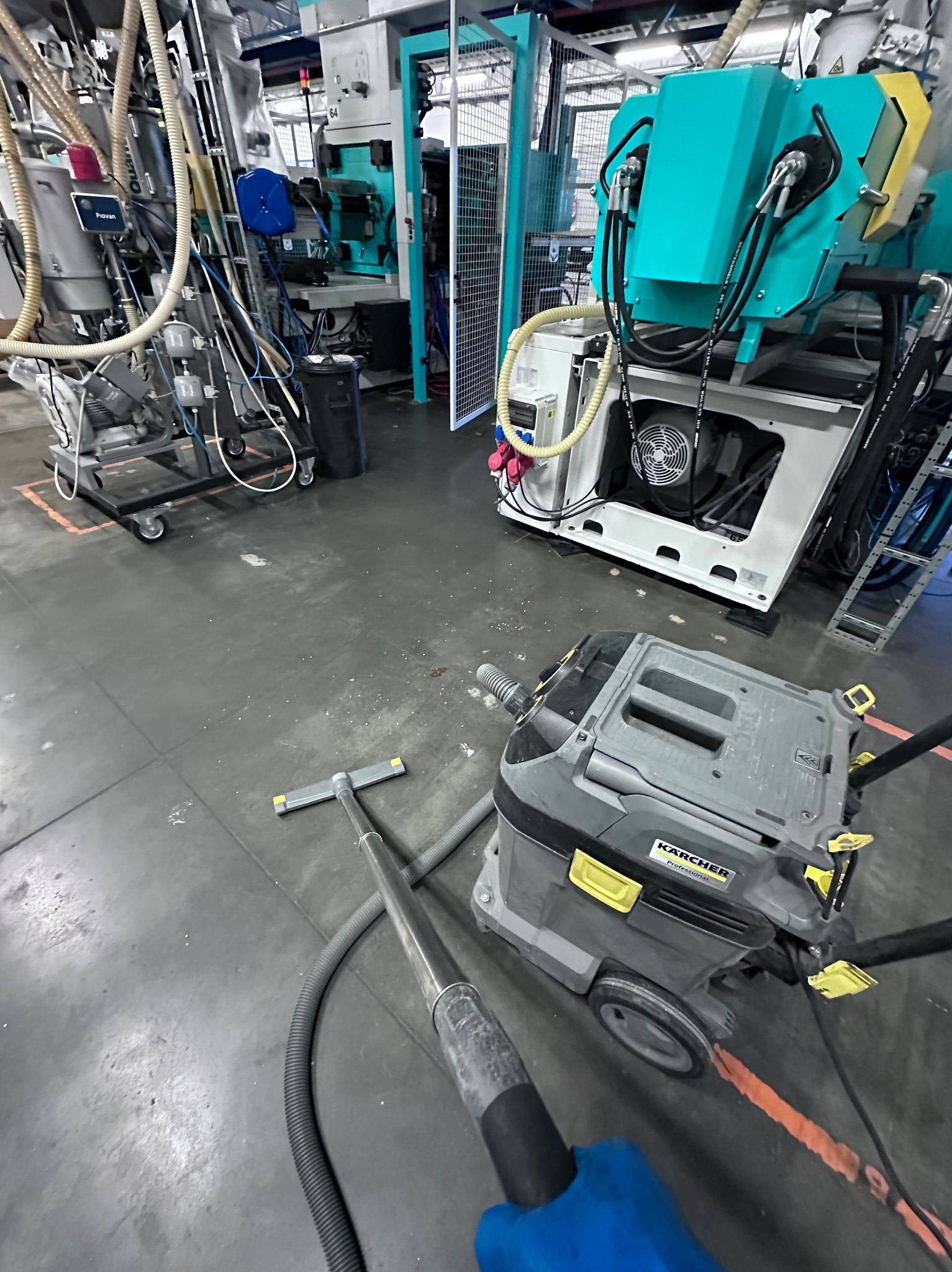 Przemysłowy odkurzacz Karcher Professional na szarej betonowej posadzce hali produkcyjnej, w tle maszyny i instalacje.