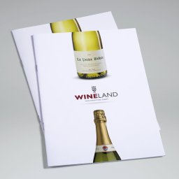 idesign JAROSŁAW JAWORSKI - Dwa identyczne, zszyte foldery reklamowe Wineland z fotografiami butelek wina białego i musującego na białym tle, leżące na szarym podłożu.