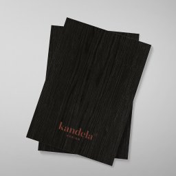 idesign JAROSŁAW JAWORSKI - Dwa czarne arkusze papieru z fakturą drewna i pomarańczowym logo 'kandela DESIGN' w lewym dolnym rogu, ułożone na jasnoszarym tle.